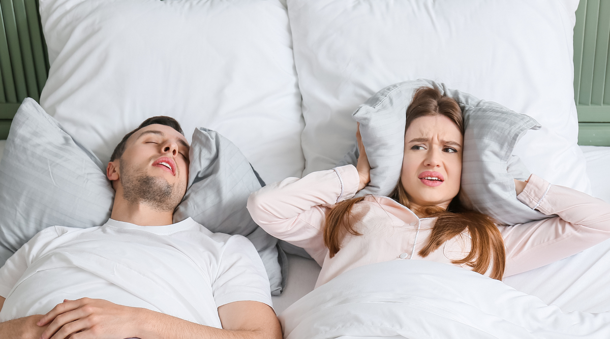 Mann schnarcht im Bett, Partnerin hält sich Ohren zu