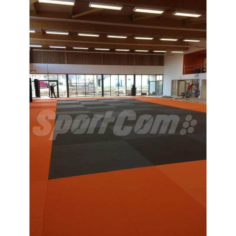 SportCom Judo-Tatami Reisstroh 2 × 1 m, 5 cm, glatte Unterseite, orange Fläche mit grauer Zone in Halle mit Fensterfront