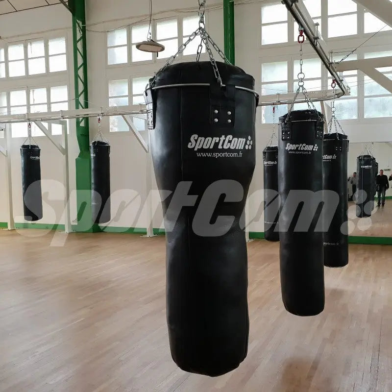 SportCom Kunstleder-Uppercut-Sandsack, mehrere Säcke hängen in einer hellen Trainingshalle mit Holzboden