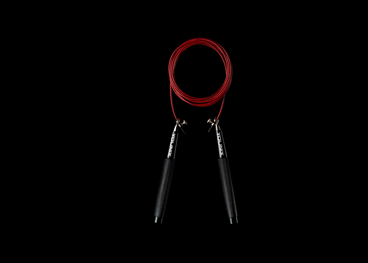 Younix Skill Rope Springseil mit rotem Seil und schwarzen Griffen, hängend vor schwarzem Hintergrund