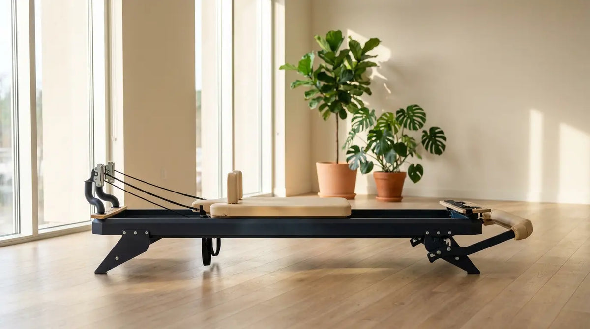 Reformer Pilates di alta gamma con telaio in acciaio, situato in una palestra luminosa e moderna con pavimento in legno e ampie finestre