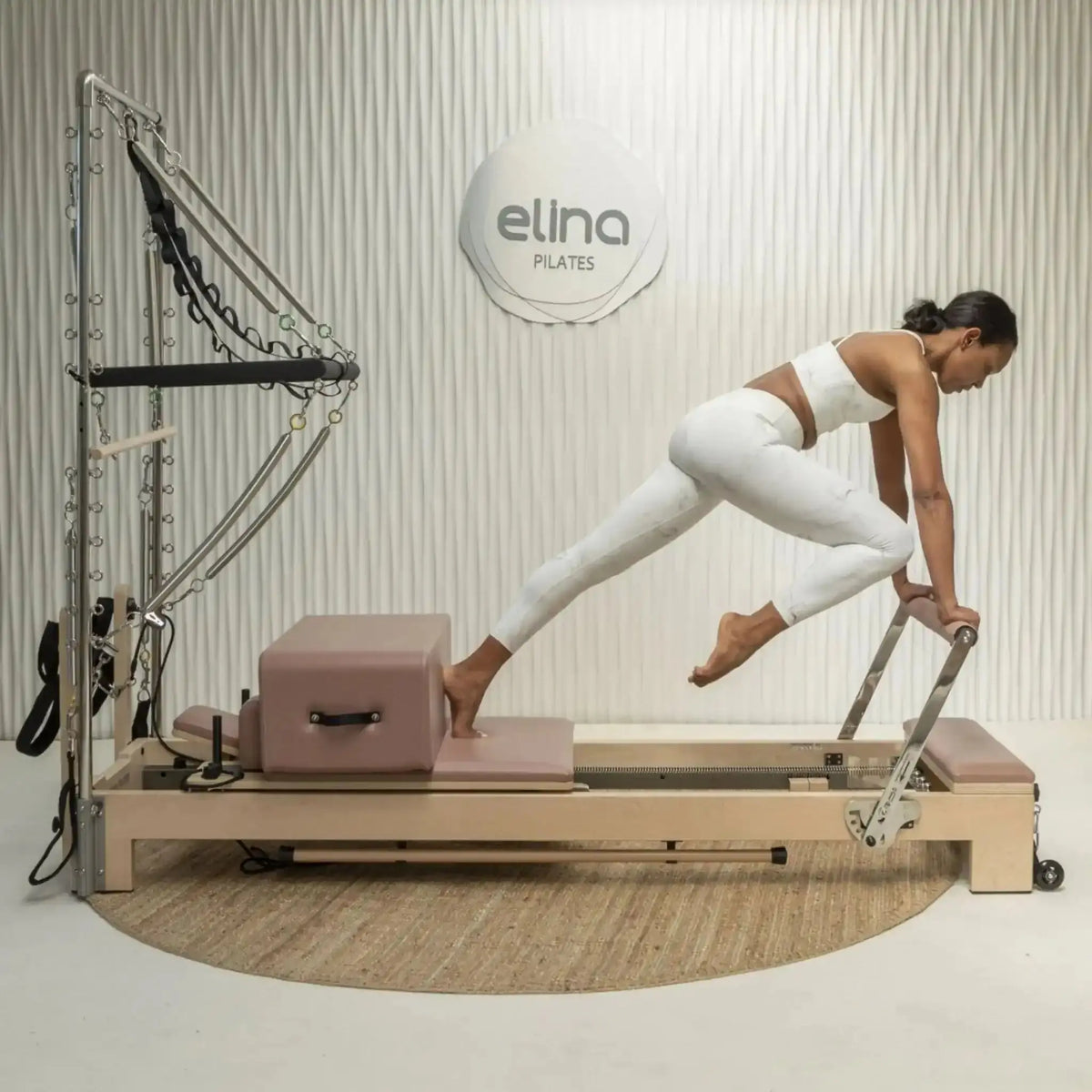 Elina Pilates Lignum Reformer mit Tower aus Holz, Frau trainiert im Studio in der Streckung auf dem Schlitten