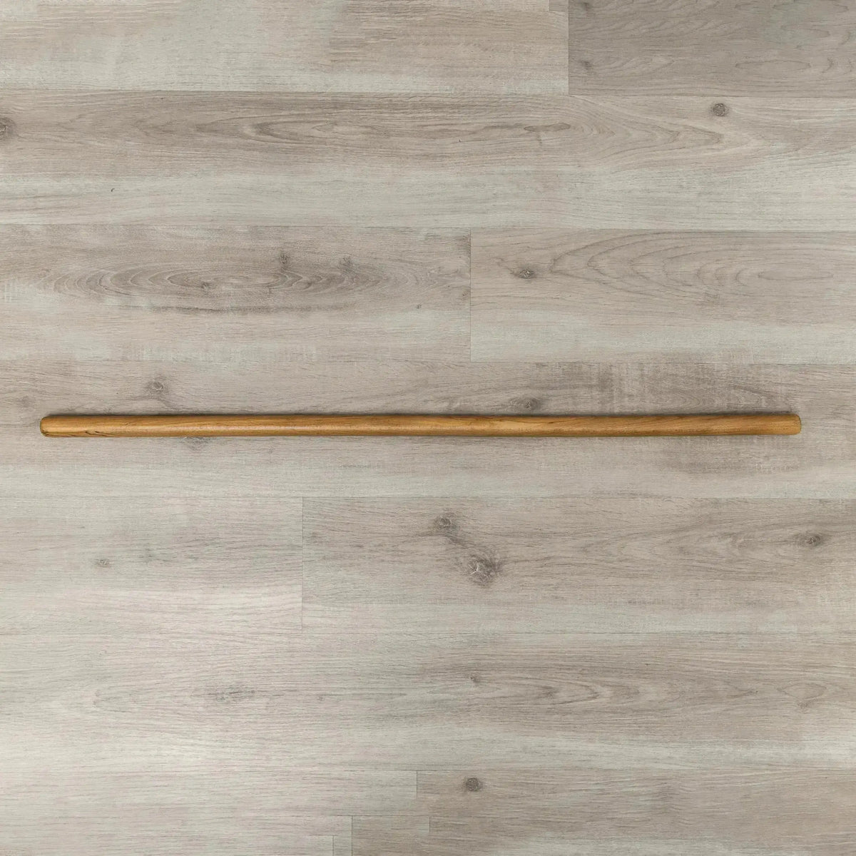 Hegren Pilates Wooden Stick 1,10 m aus Eiche, ganzer Stab liegend auf hellem Holzboden