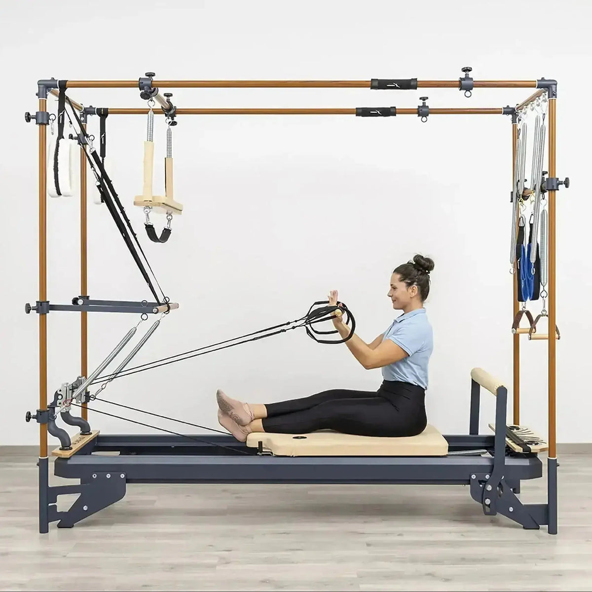 Hegren Pilates Wooden Stick 1,10 m aus Eiche, Frau sitzt auf dem Cadillac-Reformer und zieht den Stab an Seilen