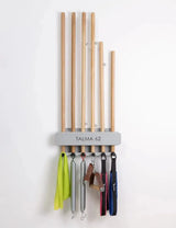 Hegren Stick Stand Wandhalter an weißer Wand mit sechs Holzstäben oben und Bändern an den Haken darunter