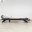 Hegren TALMA 62 Reformer mit Box und Jumpboard in Seitenansicht mit dunklem Rahmen und beigen Polstern auf hellem Holzboden