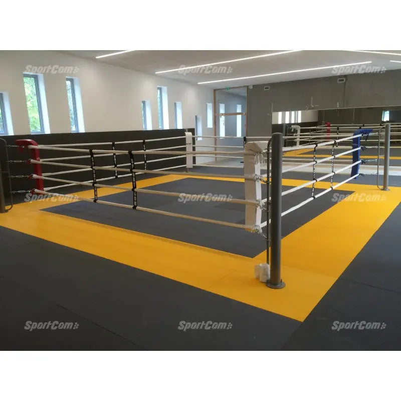 SportCom Bodenanker-Boxring mit Stahlpfosten auf gelb-grauer Mattenfläche in einer hellen Halle