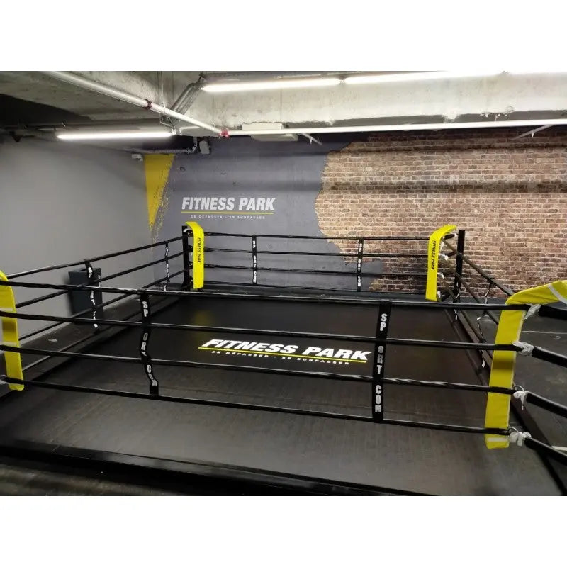 SportCom Boxring-Individualisierung: Bodenring mit gelbem Schriftzug und gelben Ecken vor Backsteinwand
