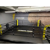 SportCom Boxring-Individualisierung: Bodenring mit gelbem Schriftzug und gelben Ecken vor Backsteinwand
