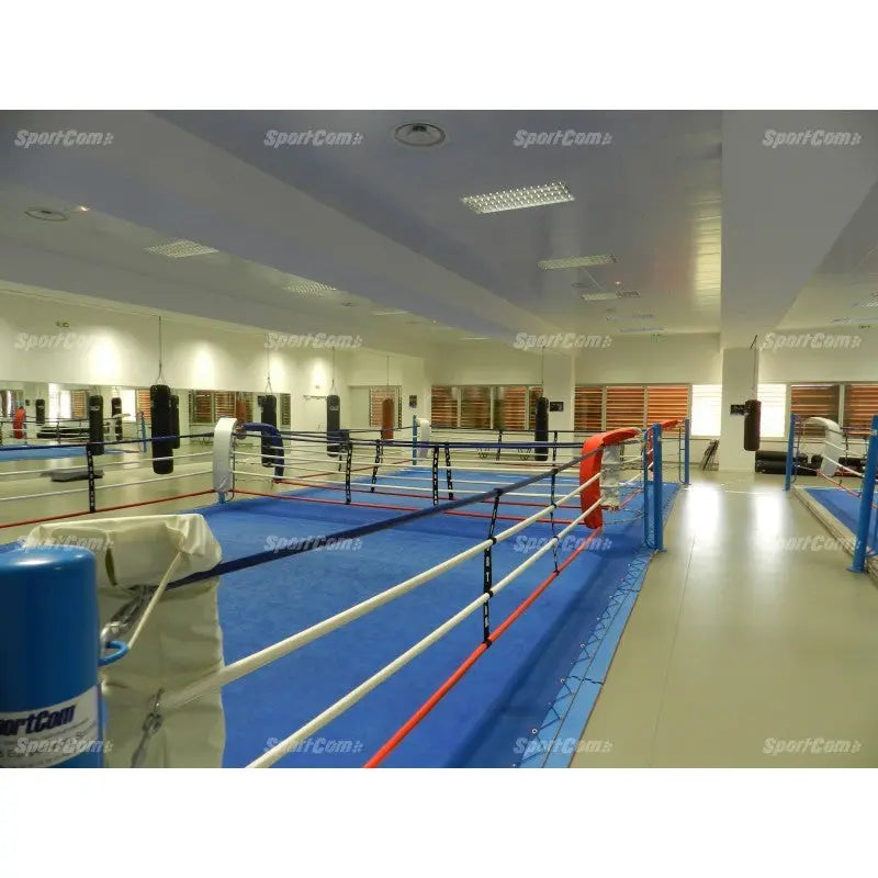 SportCom Doppel-Boxring Bodenpfosten mit Spannseilen, in einer Halle mit blauem Boden und Boxsäcken