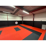 SportCom Flexi-Wall Wandschutz von Dollamur in Schwarz über orange-schwarzen Matten im Dojo