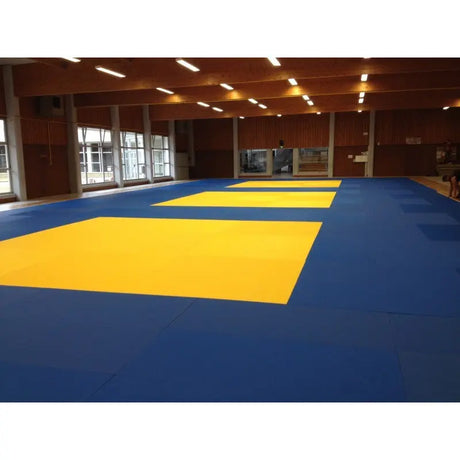SportCom Judo-Tatami Reisstroh 1 × 1 m, 5 cm, rutschfeste Unterseite, blaue Fläche mit gelben Feldern unter Holzdecke