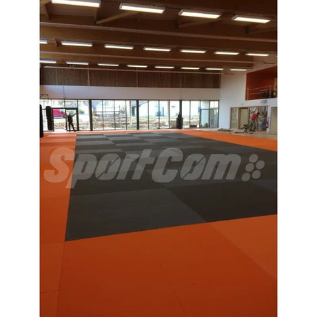 SportCom Judo-Tatami Reisstroh 1 × 1 m, 5 cm, rutschfeste Unterseite, orange Fläche mit dunklem Feld in heller Halle