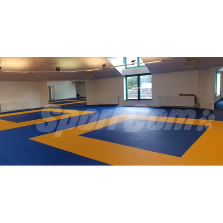 SportCom Judo-Tatami Reisstroh 2 × 1 m, 5 cm, glatte Unterseite, blau-gelbe Fläche in heller Halle mit Fensterfront