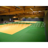 SportCom Judo-Tatami Reisstroh 2 × 1 m, 5 cm, glatte Unterseite, gelbe Fläche mit grünem Rand in einer Holzhalle