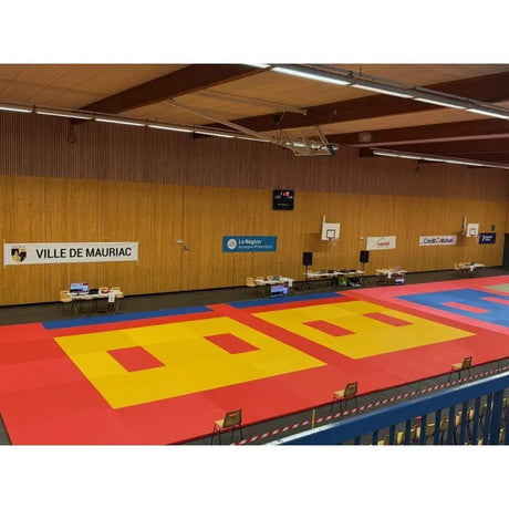 SportCom Judo-Tatami Reisstroh 2 × 1 m, 5 cm, glatte Unterseite, rote Fläche mit gelben Kampfzonen in großer Sporthalle