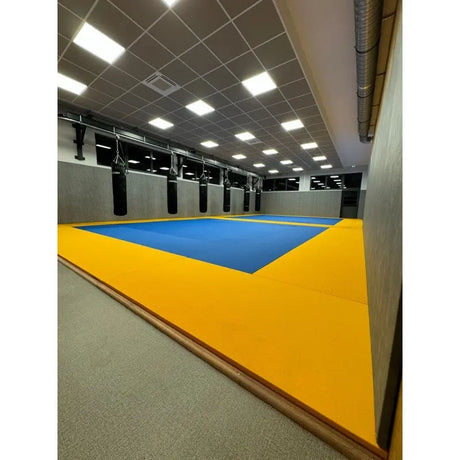 SportCom MMA-Tatami Glattfinish 1 × 1 m, 5 cm, glatte Unterseite, erhöhte gelb-blaue Fläche in hoher Halle