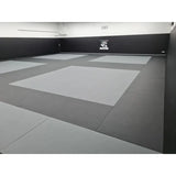 SportCom MMA-Tatami Glattfinish 1 × 1 m, 5 cm, glatte Unterseite, Studio mit hellgrauen Feldern auf dunklem Grund
