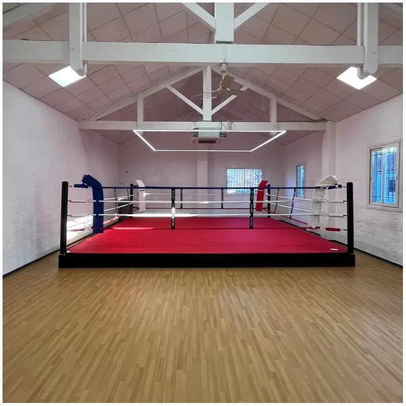 SportCom Pro-Trainingsboxring mit 30 cm Podium, mit rotem Boden in einer hellen Halle mit Holzdecke