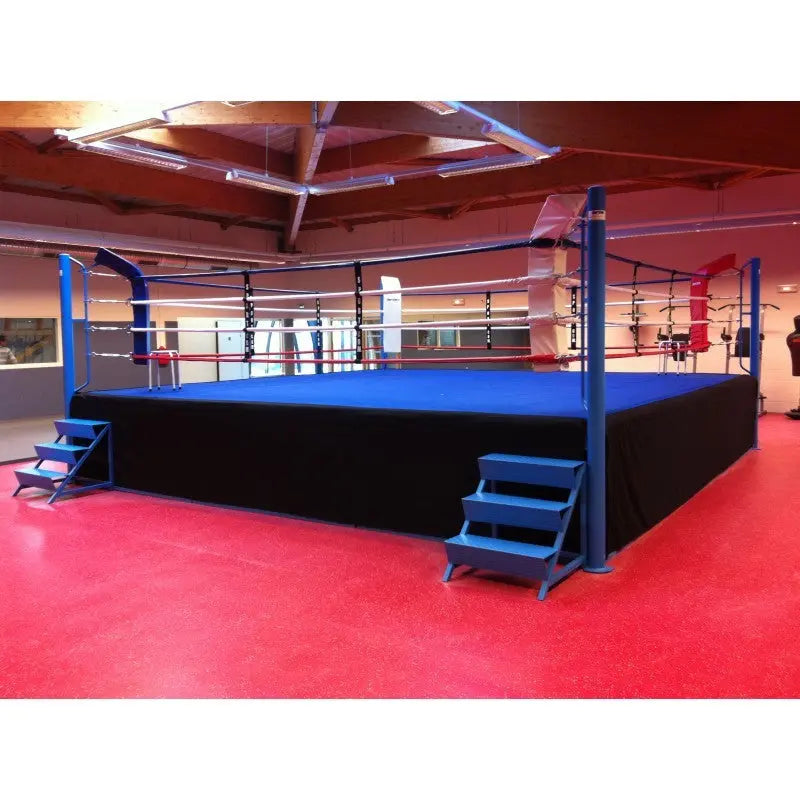SportCom Pro-Wettkampf-Boxring mit 1 m Podium, mit blauer Ringfläche und Treppen auf rotem Boden
