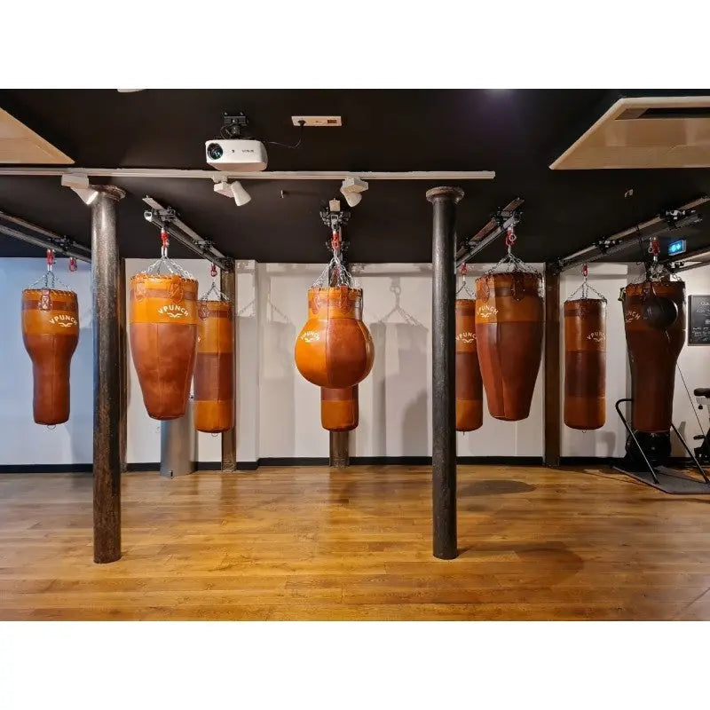SportCom Vintage-Uppercut-Sandsack Echtleder in einem Boxstudio mit mehreren hängenden Ledersäcken
