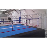 SportCom Wettkampf-Boxringseil mit Hülle, Boxring mit blauer Fläche und weißen Seilen in einer Halle