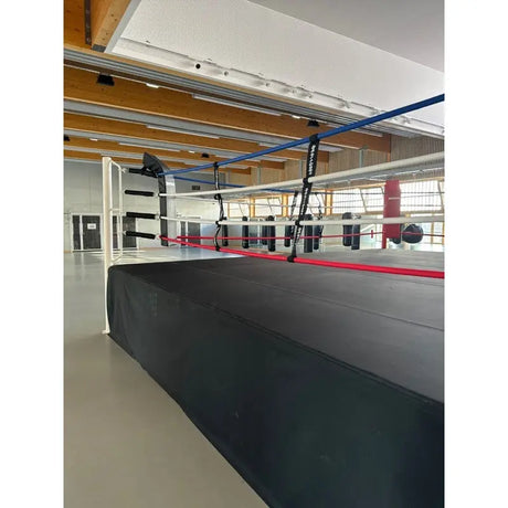 SportCom Wettkampf-Boxringseil mit Hülle, erhöhter Boxring mit blauen, weißen und roten Seilen in heller Halle